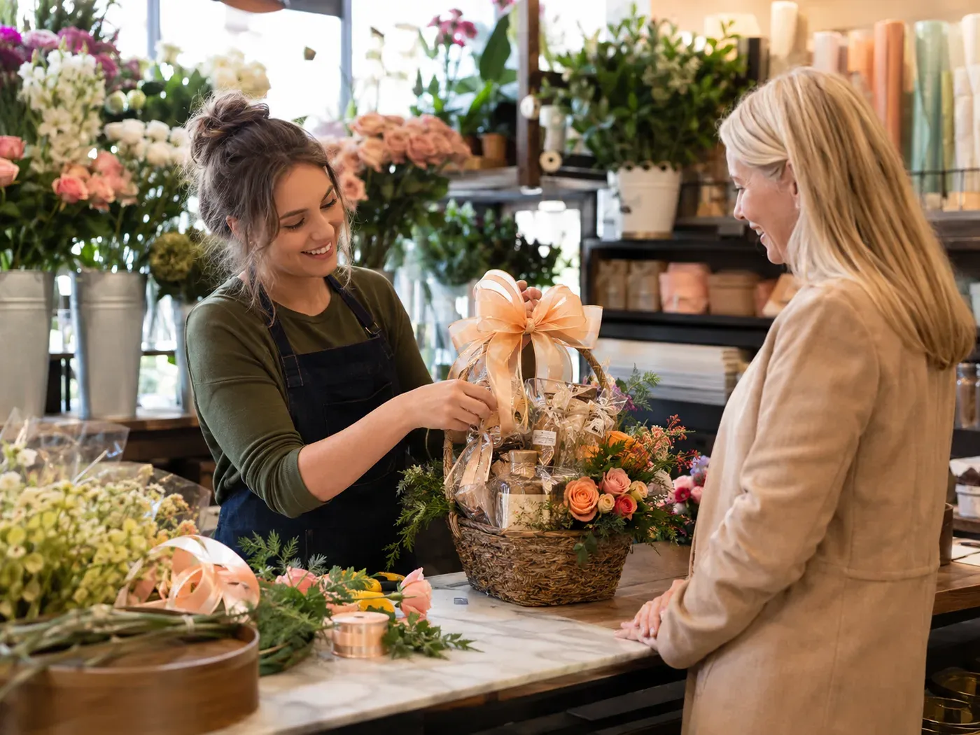 Eine Frau übergibt einer anderen Frau lächelnd ein Geschenk in einem Blumenladen