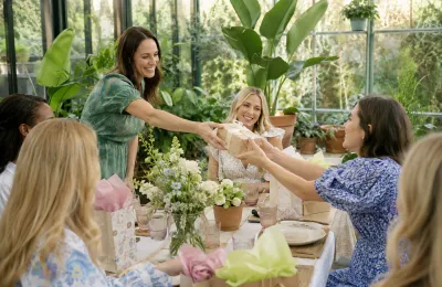 Eine Gruppe von Frauen überreicht sich bei einem Gartenbrunch fröhlich ein Geschenk