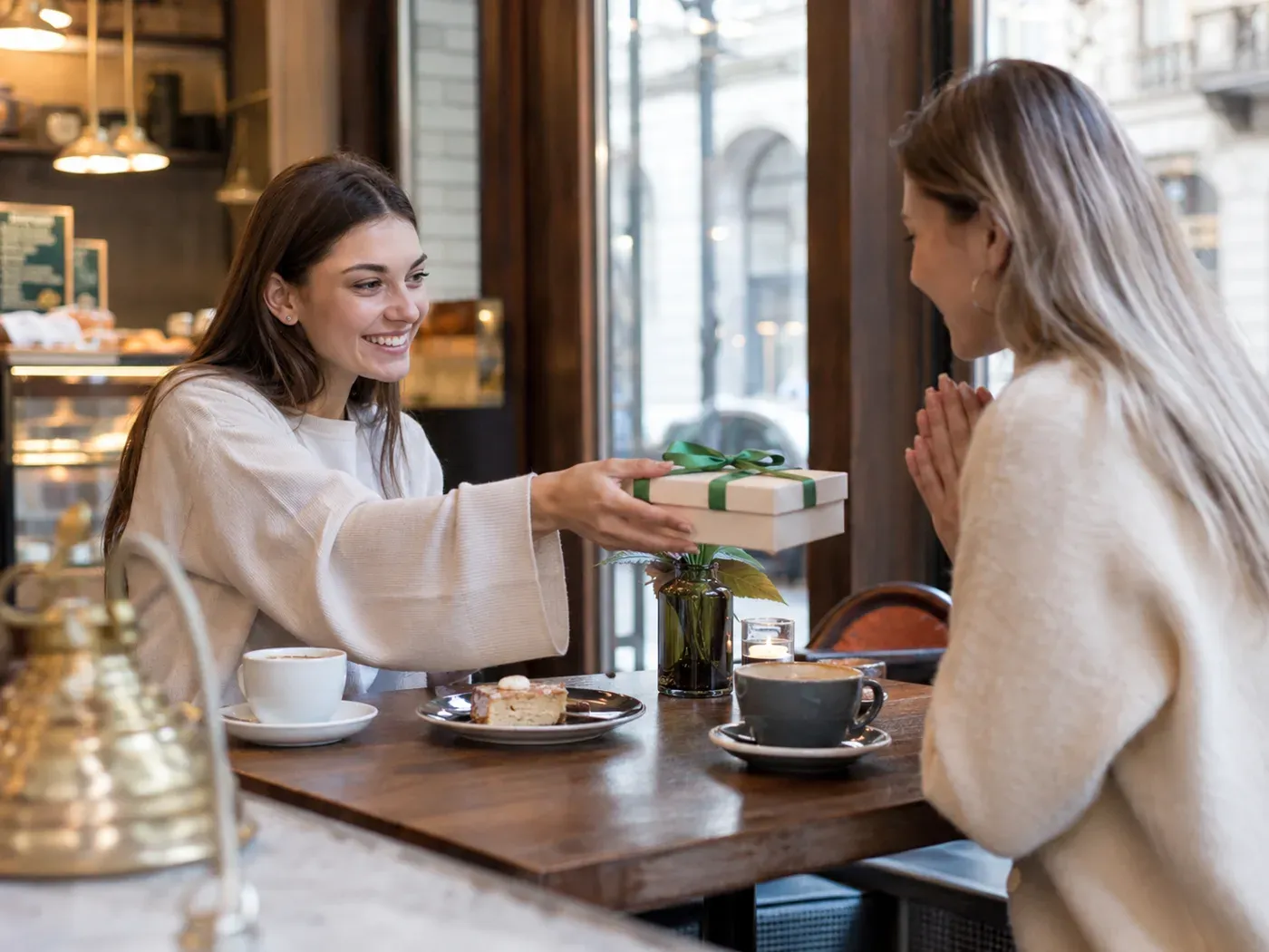 Eine Frau überreicht ihrer Partnerin ein liebevoll verpacktes Geschenk in einem Café