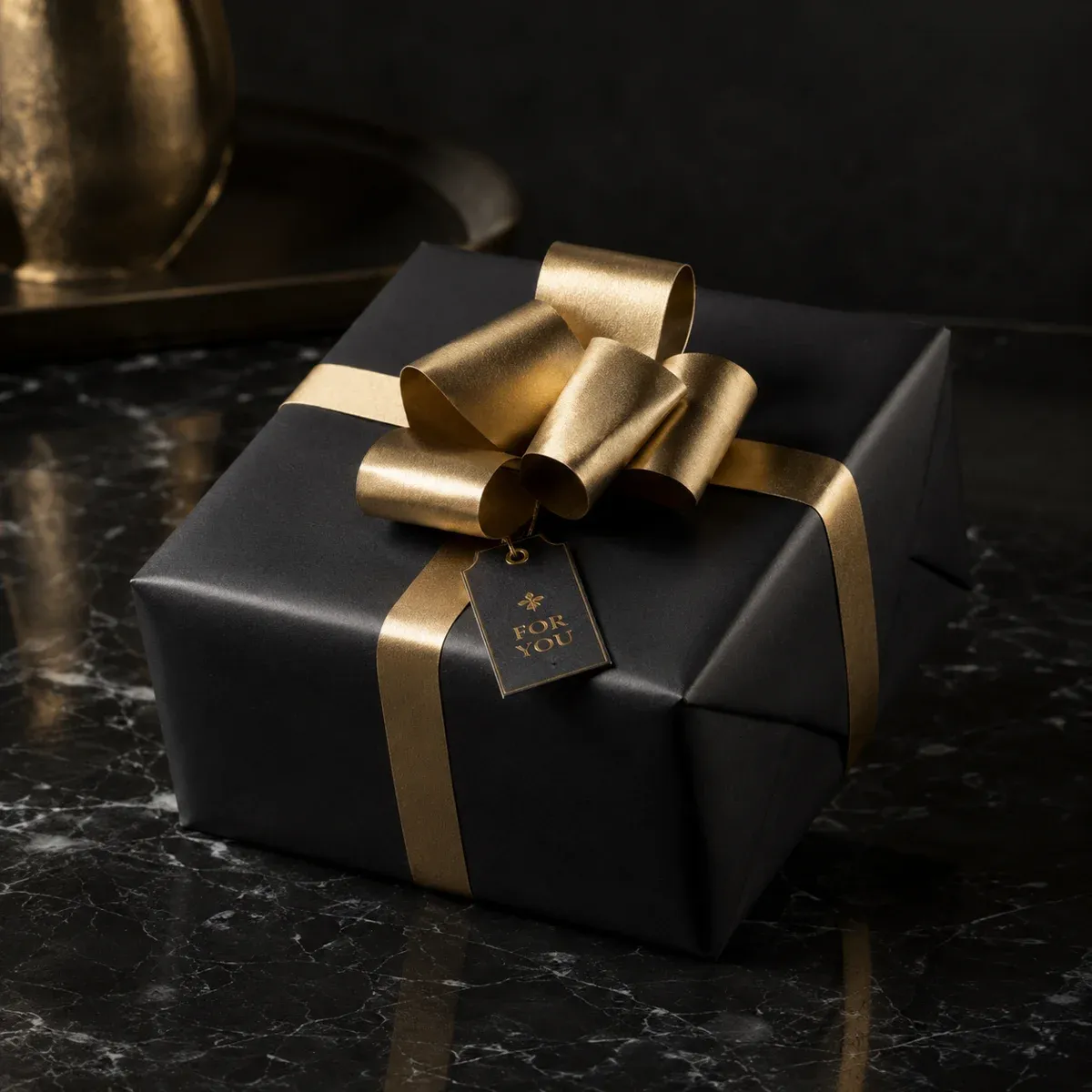 Elegant in Schwarz und Gold verpacktes Geschenk mit Schleife auf dunklem Marmoruntergrund