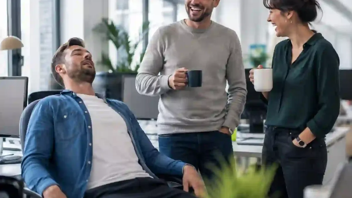Ein Kollege überreicht lächelnd ein Geschenk mit Namensschild an eine Kollegin im Büro
