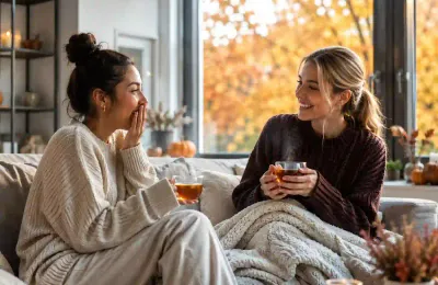 Zwei Freundinnen trinken gemeinsam Tee auf dem Sofa, im Hintergrund bunte Herbstblätter