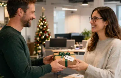 Ein Kollege überreicht einer Kollegin ein Wichtelgeschenk mit dem Namensschild 'Anna' im weihnachtlich dekorierten Büro